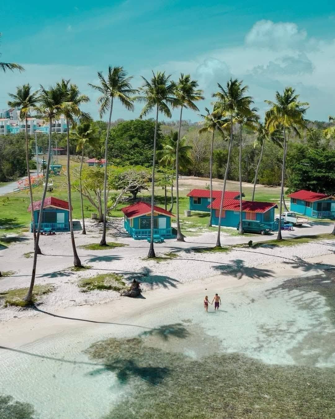 Pareja caminando en el agua cristalina frente a las cabañas de Villa La Mela